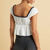 White top with black trim worn by a person on a beige background